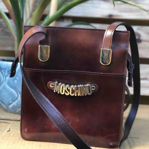 Vintage moschino läderväska! Skulle gissa att denna är från 90/tidigt 00-tal. Relativt korta väskband vilket gör att den sitter snyggt på kroppen (på mig som är 167 går den ner till precis under midjan)