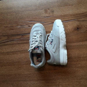  - Fila Disruptor i bra kvalitet. Skorna är i 37 (woman size).  skorna har vita snören. 2 Fila märken på sidan av skorna samt en på hälen och i skorna, på sulan. Fila märket finns också på tungan av skorna och ett litet märke vid bandet som håller ihop skosnören. Inget märke är skadar och syns tydligt på skorna. I skorna finns det ett mönster som knappt syns när skorna används. Dom här skorna rekommenderas att användas sneakers/vardagskor