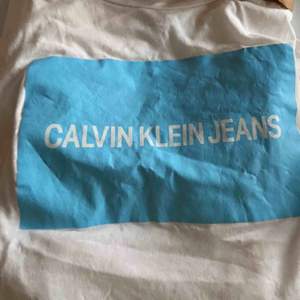 Vit t-shirt med blått tryck från Calvin Klein! I super skick förutom lite skrynklig, vilket lätt går att fixa. Köpt för Nelly för något år sen, men knappt använd. Är storlek S men passar XS-M också beroende på önskad passform.   !! Frakt ingår ej !!