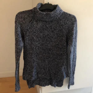 Stickad tröja från Vero Moda  - Supermysig stickad tröja i färgen mörkblå/grå. Längre baktill och med en liten polokrage. 