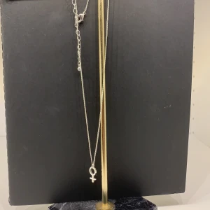 Halsband kvinnomärket - Ett superfint oanvänt halsband i silvrig färg med kvinnomärket. Köparen står för frakten. Fraktar endast.