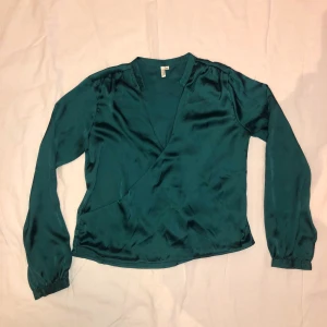 Satin blus - Mörkgrön blus från Nelly, i siden material. Väldigt urringad, men enkelt löst med två stygn eller säkerhetsnål. Strl 40, säljer för 50 kr + frakt :)