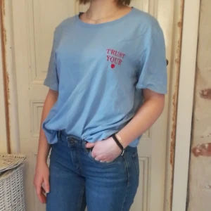 Ljus blå T-shirt med broderi - Ljus blå thisrt med röd broderad text. 100% Bomull 