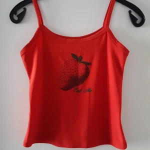  - Rött linne med en jordgubbe och text på. Står ej storlek men ca som XS/S och är väldigt stretchig. Fraktkostnad blir 44kr.