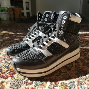  - Svarta sneakers med hög sula och vita och silvriga detaljer. De är väl använda men är fortfarande i gott skick! OBS, katt i hemmet. Köparen står för frakt. 