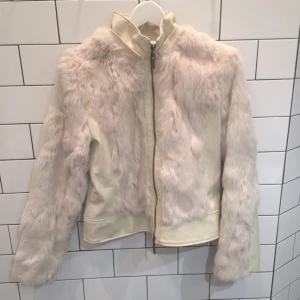  - Söt fest- och vårjacka i mörkvitt konstläder med stora dekorationer av vit kaninpäls (100% äkta). Inga hål eller fläckar i pälsen, några väldigt små sprickor i konstlädret som jag inte tycker stör utan är snygga då de ger jackan en vintage- / patinerad look.

Insida i satin (inga hål), liten ståkrage och stängs med fullt fungerande dragkedja. 

Köptes på Judits secondhand vid Mariatorget för cirka ett år sedan, då för 1200 kr. 

Maila eller smsa gärna för fler bilder!