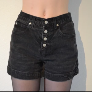 - Jeansshorts i svart semin med hög midja och tryck-knappar.