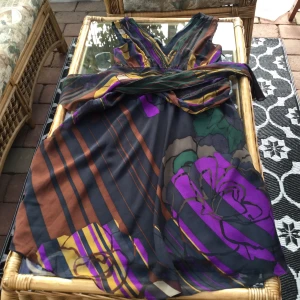 Snygg festklänning i  silke - Festklänning i läckra färger matrial silke dragkedja i sidan 32 cm lång tunt foder i svatt v- ringad fram och bak knytband bak kjolens vidd är 1.50 cm hela klänningens längd 1.08 kemtvätt fint skick nypris 1400:- tar swish