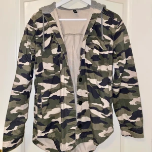 Militärjacka med grå luva - Kommit till användning endast 2 gånger. Storlek 32 men passat även för en 34. Jackan stängs med svarta knappar, har fickor och luva.