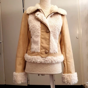 Beige päls jacka vår/höst - Kort beige jacka i oäkta päls/mocka. Dold dragkedja bakom flärpen som knäpps med tre söta knappar. Passar bra när hösten snart är på väg. Är varm och skön. Använd 2-5 ggr, som ny. Frakt 70 kr.