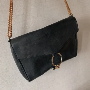 Svart axelremsväska med gulddetaljer - Svart axelremsväska i imitationsläder med gulddetaljer. Priset är inkl frakt