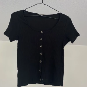 Svart croptop - Ribbad croptop med knappdetaljer, obs! knappt går ej att öppna! Nyskick. Hämtas i Sundbyberg, annars står köparen för frakt.