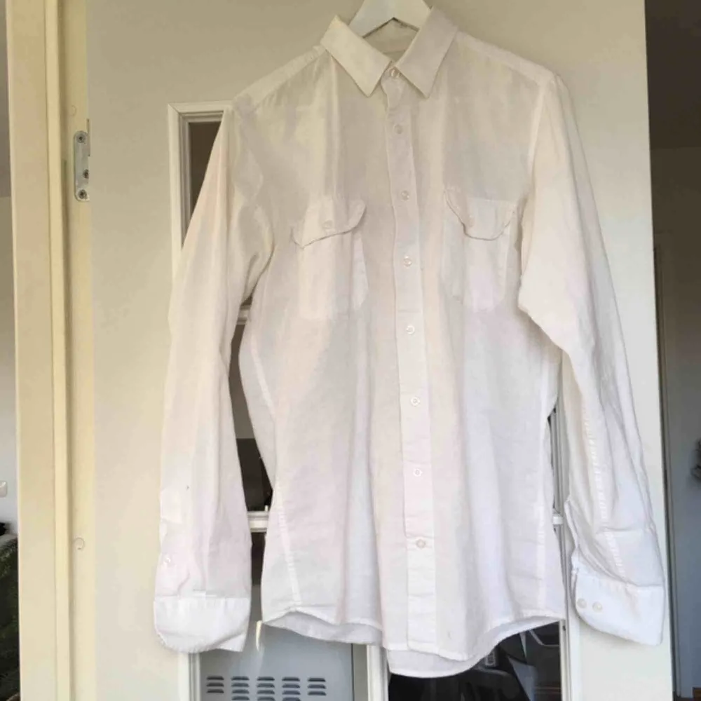 En vit skjorta i herrmodell. Den har 2 bröstfickor. . Skjortor.
