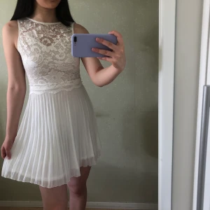 Plisserad klänning - En fin plisserad klänning med en öppen rygg. Klänningen består delvis av spets med olika blommönster. Endast använd en gång och då självklart sparsamt använd🥰