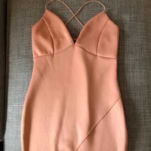 Figurnära klänning - Peachrosa, figurnära klänning med tunna korsband och dragkedja i sidan. Liten slits, se andra bilden. Aldrig använd, lapp kvar! AX Paris, köpt fr Nelly.