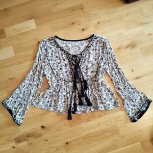 Blommig blus - Supersöt blommig blus i vitt och mörkblått med vida ärmar och snygg snörning framtill. Blusen har ett lätt rynkat midjeparti och tunna, flowiga material som ger en bohemvibe. Storlek 34 men passar även 36