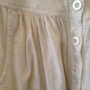 Vit klänning med små blommiga broderier och knappar.  - Vit klänning med små blommiga broderier och knappar. 