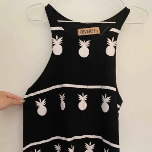  - Svart top med vit tryckt ananasdesign. Brottarstil, A-linjeformad.   Köparen står för porto