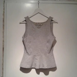  - Snygg grå topp från Bikbok i storlek M.  Högurringning framtill prytt med stenar i vitt och gula pärlor. Med djup V-ringning i ryggen. Använd en-två gånger så är i nyskick! Riktigt snygg och fin som festtopp. Pris 30kr. Betalas med swish🎉