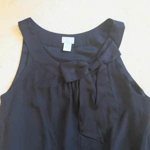  - Svart kort klänning med sidenrosett på vänster sida av urringningen 