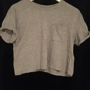 En grå t-shirt med en ficka på bröstet, väldigt stilren och fungerar till allt, använd få gånger (priset kan alltid diskuteras)
