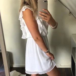 Vit klänning  - En jättefin vit klänning (strl XS) med resårband i midjan, vilket gör att du kan välja hur du vill att den ska sitta. Dne har volanger på ”axlarna” vilket är en fin detalj! Köparen står för frakten!🤍