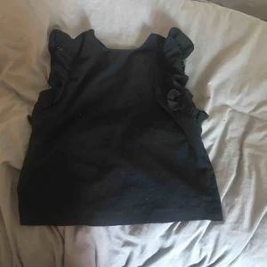  - Armlös tröja med volanger på båda sidorna av ärmen.