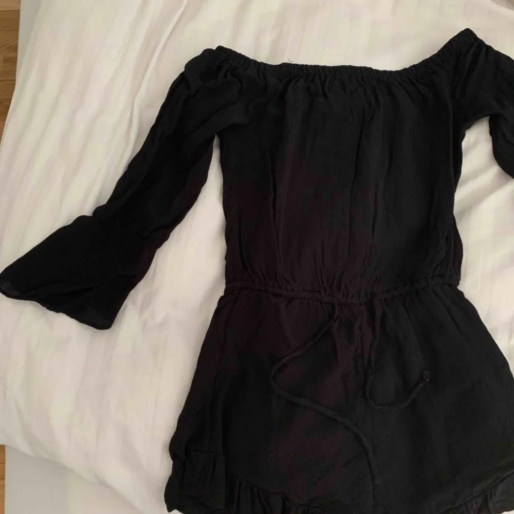 Svart playsuit/jumpsuit. Off shoulder. Lite finare material,  luftig, knytning i midjan. Ärmen är en trekvartsärm. Lite volanger på slutet av playsuiten vid benen samt ärmar. Säljer den då den tyvärr blivit för liten för mig. Endast använd tre gånger. Övrigt.