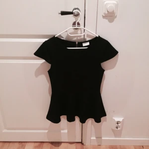  - Svart figursydd topp från Vila. Använd 3 gånger, i mycket fint skick. I tjockare material (70 % viskos). Mycket fin ringning och dragkedja i ryggen. Sitter mycket fint på, tight i midjan och vidare vid höften. Kan skicka fler bilder!