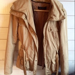  - Snygg beige kappa med fodrad uttagbar väst och luva. Gulddetajler och skärp i midjan.  Från Zara.  Passar XS-M Fint skick.  