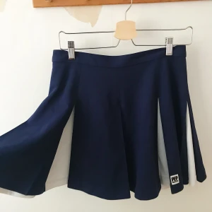 Cheerleaderkjol s. S-M - Vippig Cheerleaderkjol i marinblått och vitt. Storlek 36/38. 