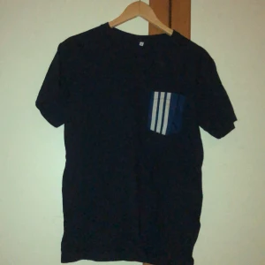 Blå t-shirt  - En blå t-shirt köpt på beyond retro. Adidas fickan är påsydd från tidigare. Det står storlek XS men skulle säga att den är i S/M