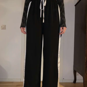 Byxor - Ett par riktigt härliga byxor i riktigt fin skick! Dem är svarta med vita ränder på sidorna, man får en fin figur i byxorna och dem kan knytas framtill med snörning! Högmidjade. Jag köpte dem på Nelly.com 