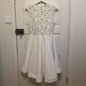  - Vit klänning. Har en plastring i kjolen för att ge den mer form. Överdelen är mesh med broderi. Knälång på mig som är 176. Felfri. Fraktkostnad tillkommer.