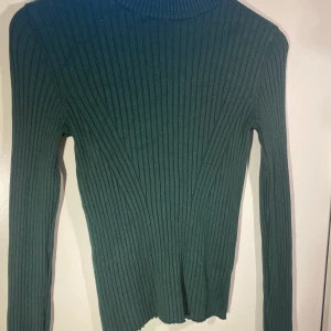 Grön tröja  - Mörkgrön ribbad tröja som är lite figursydd. Fint mönster i materialet och perfekt under en t-shirt eller som den är