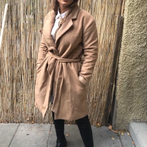 Beige kappa  - Använd kappa. Lite nopprig och en ljusare missfärgning på insidan av kragen, säljes därför billigt. Frakt 95 kr.