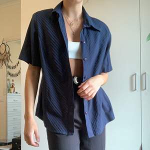 En mörkblå kortärmad skjorta med mönster i tyget på framsida och har axelvaddar. Aldrig använd. Storlek 44 men passar som en 36. 