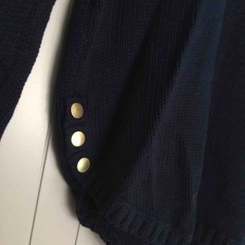En mörkblå stickad tröja med guldfärgade knappar längst ner på sidorna. Använd 1 gång. Storlek XS men passar S-M beroende på hur man vill ha passformen då den är lite längre. Är 162cm lång och den går ner till nästan mitten av låret. (Borås/Göteborg). Tröjor & Koftor.