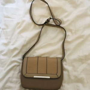 Beige väska  - Beige axelremsväska, ungefär 20 cm x 25 cm.  100kr inklusive frakt 