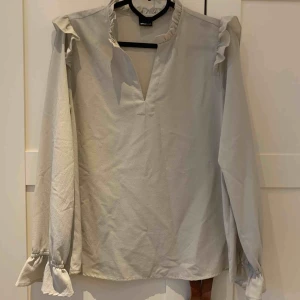  - Blus med volang från Gina Tricot. Vidare nedtill, smock i ärmslut. Grågrön i färgen.