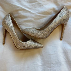 Nya Glittriga klackskor - Festliga och snygga klackskor från Asos. Aldrig använda!! Jättebra skick. De är guldglittriga men som ni ser på bilerna ser de mer champagne/silver färgade, den perfekta färgen verkligen. ||||| Det står ingen storlek på skorna förutom 9, jag skulle säga att de är 38/39