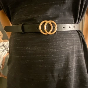 Svart bälte i guld detalj - Jättefin svart bälte i fejk läder i en guld detalj, modern och passar till allt möjligt. Stick ut extra mycket med denna fina bälte. 