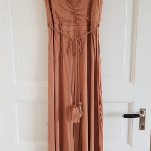 H&M byxdress  - Byxdress från H&M med vida ben och skärp med tofsar. Mycket bra skick, använd en gång. Inköpt kring år 2012. Normal strl. M med bra passform.