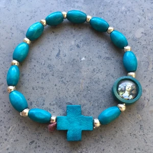  - Armband med turkosa träpärlor, kors och bild på en historisk kvinna. Armbandet är trätt på gummiband och är därför elastiskt. Inköpt på Sicilien för 2 år sen, aldrig använt.   Frakt 7 kr.  Betalas med swish, kontoinbetalning eller vis Plick.  Kolla gärna mina andra annonser också med fler smycken, kläder och väskor. Jag kan samfrakta.