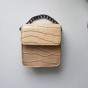  - Beige väska med kort kedja samt justerbart och avtagbart band. Nyskick, oanvänd!   Säljer även en likadan i svart. 100 kr/st men vid köp av BÅDA får du de tillsammans för 130 kr.   Du står för frakt om du inte kan mötas upp i Stockholm.