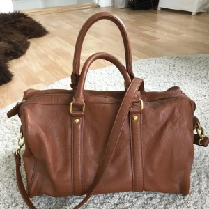  - Fin mellanstor handväska / axelremsväska från Åhléns, deras egna märke. Perfekt skick då den aldrig blivit använd. Se ena bilden för uppfattning om storlek.   Kan skickas mot att köparen betalar frakten på 55kr.