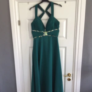  - Grön långklänning endast använd en gång. Har korsade band i ryggen med hakar och även en dragkedja på sidan. Skickas med posten mot att köparen betalar frakten.