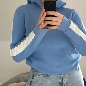 Hoodie - Ljusblå hoodie med vita streck på ärmarna. Storlek M