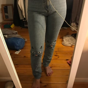 Kattjeans - Jättegulliga jeans från Monki med små broderade kattansinten. modellen Kimomo high relaxade. Storlek 26. Aldrig använda. Frakt tillkommer
