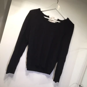  - Svart stickad tröja med "hål" och gullig rosett på ryggen. Använd men fint skick. Swishbetalning, frakt tillkommer. 